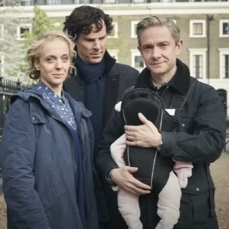Martin Freeman is holding the baby as Benedict Cumberbatch is looking at the baby.